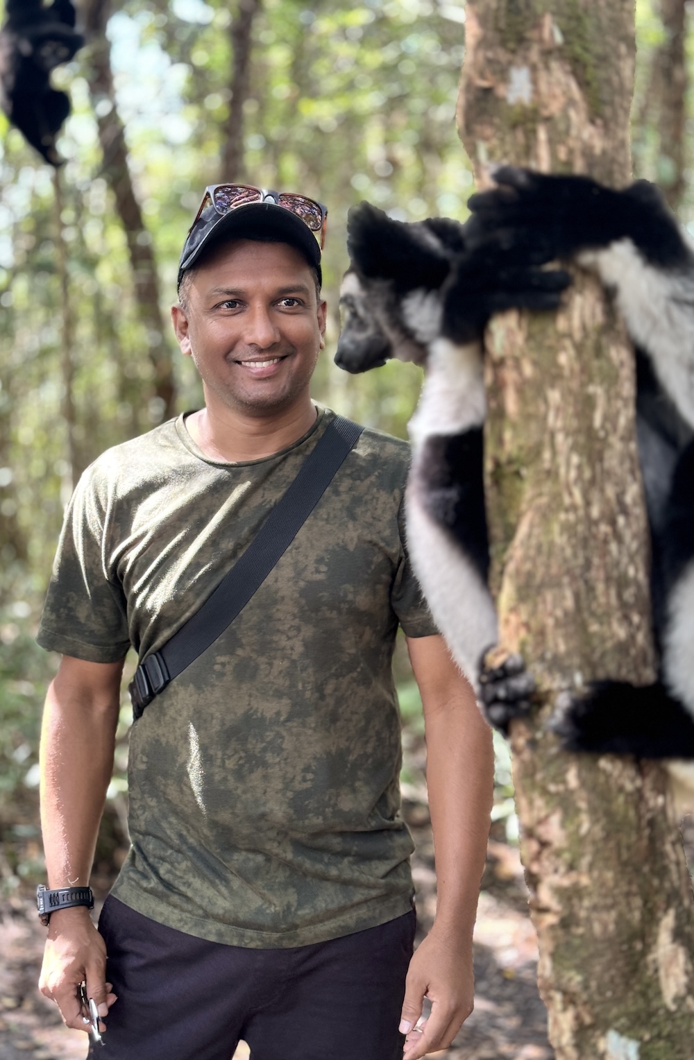 Sandeep Nanu in a rainforest in Madagascar with an Indri indri lemur on a tree behind him